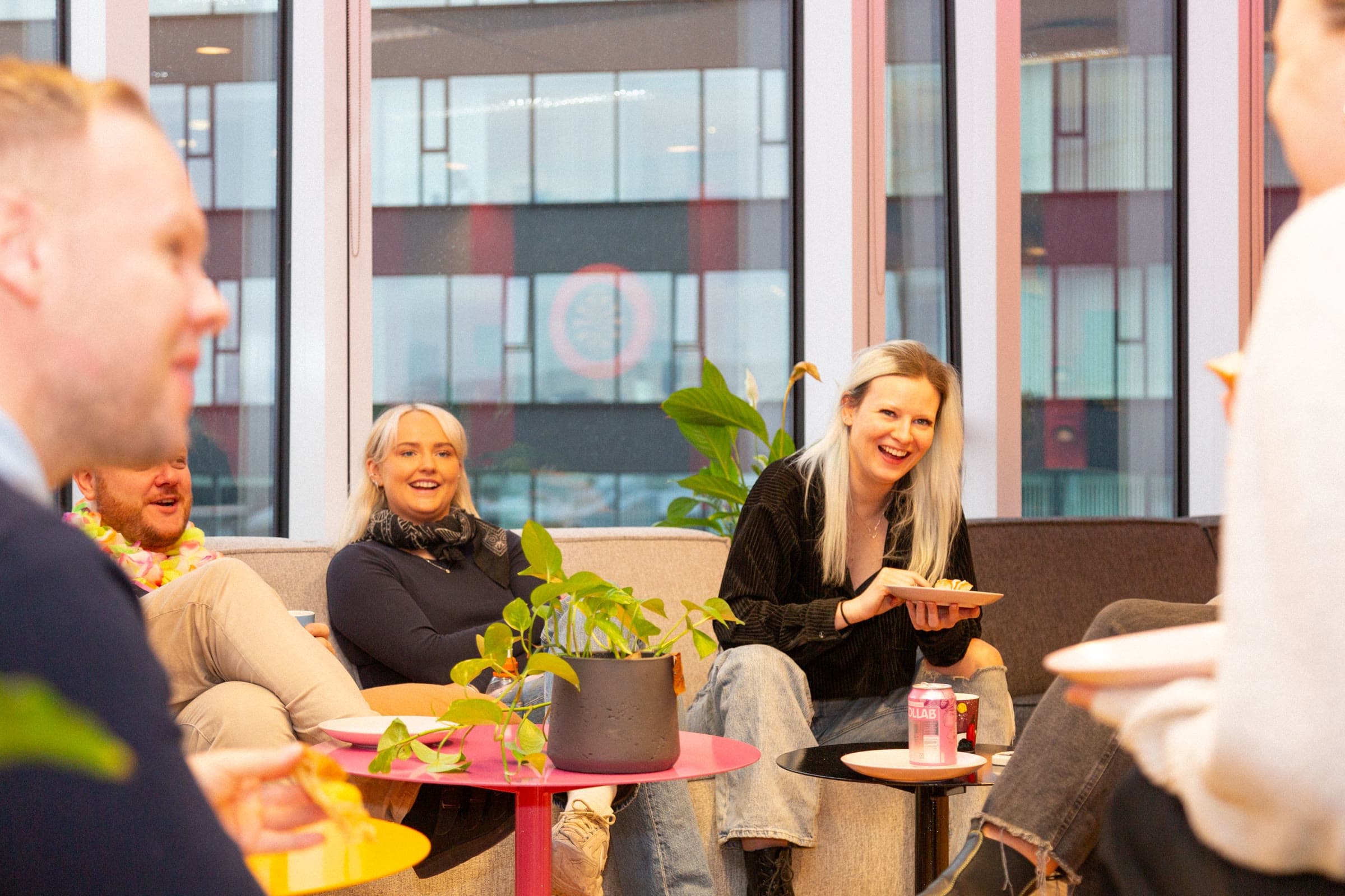 Four of the team on the office sofas with plates of food, one of them mid-laugh