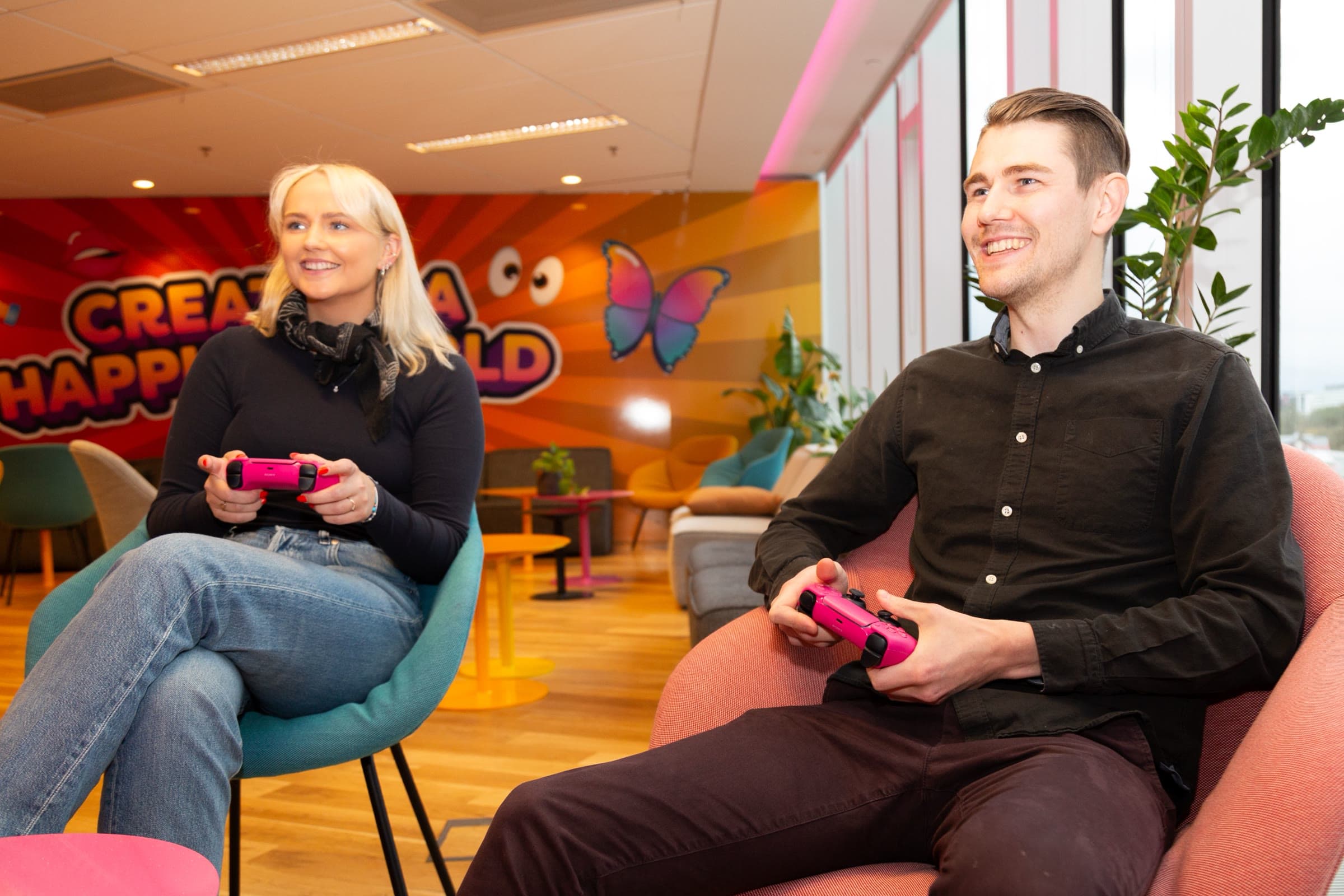 Two of the team playing a console game with pink controllers in the lounge